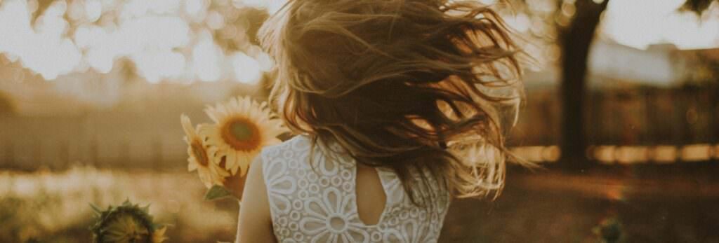 Back view of a baby girl holding a sunflower.